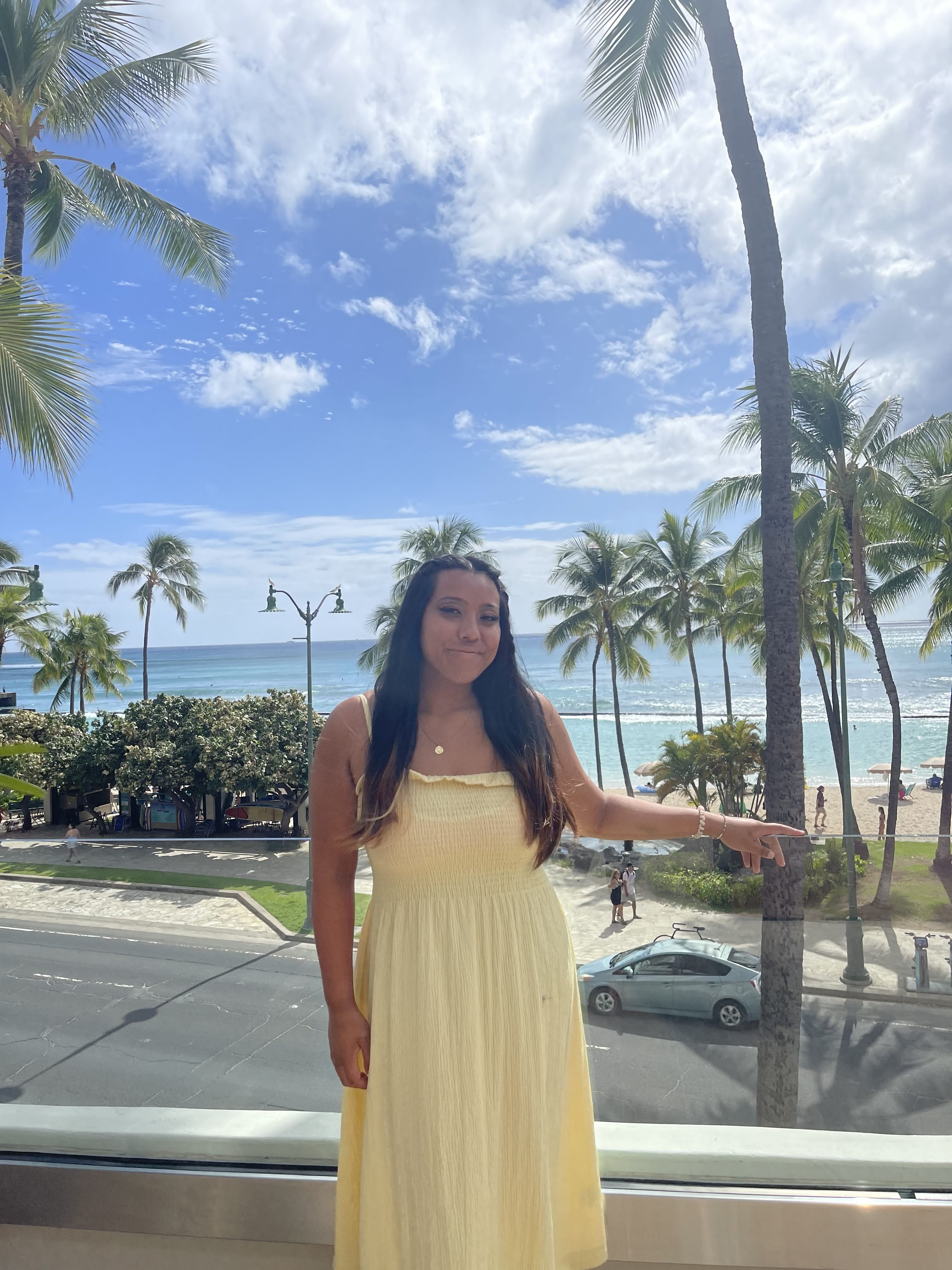 Ariel Tan stands against a clear railing while wearing a yellow dress in front of palm trees and the ocean. Tan said she plays the piano, guitar and ukulele and is in the process of creating her first EP, which she plans to release after she graduates. (Courtesy of Kristie Lin)