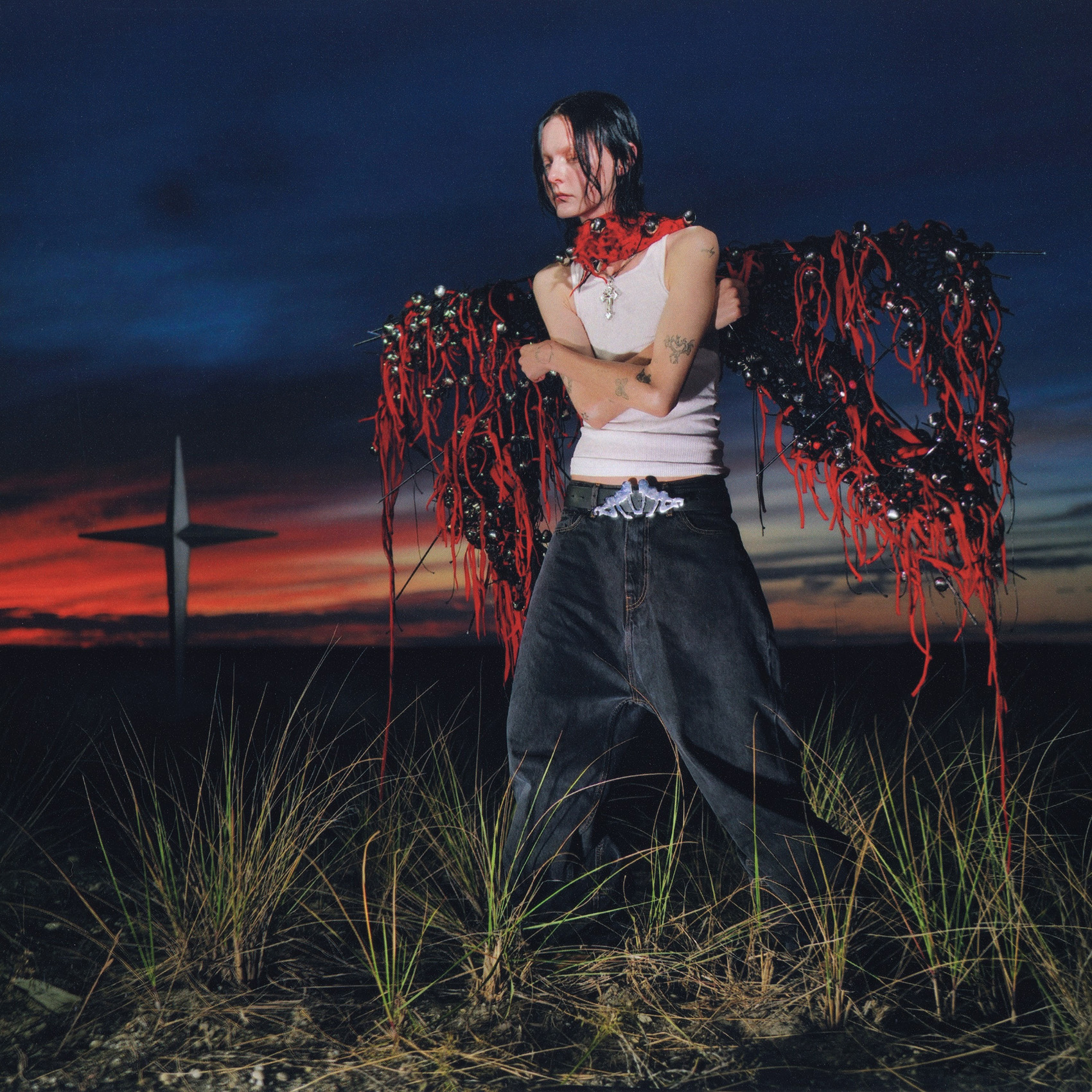 Morgan Saint wears a white tank top, red bandana and baggy jeans while standing in tall grass against a darkening sky on the cover of her 2025 album "Out Of The Blue." Saint&squot;s music includes electronic pop and lo-fi elements and was released Feb. 14. (Courtesy of 4Love)